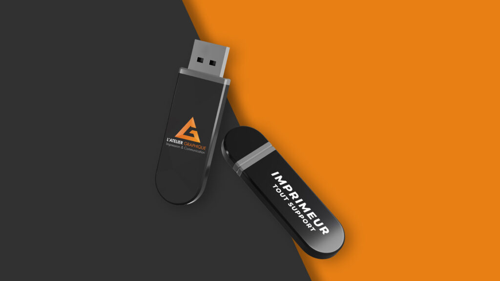 Deux clés USB publicitaires personnalisées de couleur noire avec logo imprimé sur fond orange et gris.