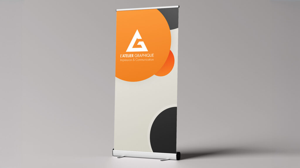 Roll-up publicitaire vertical blanc, orange et gris affichant le logo de L'Atelier Graphique sur fond neutre
