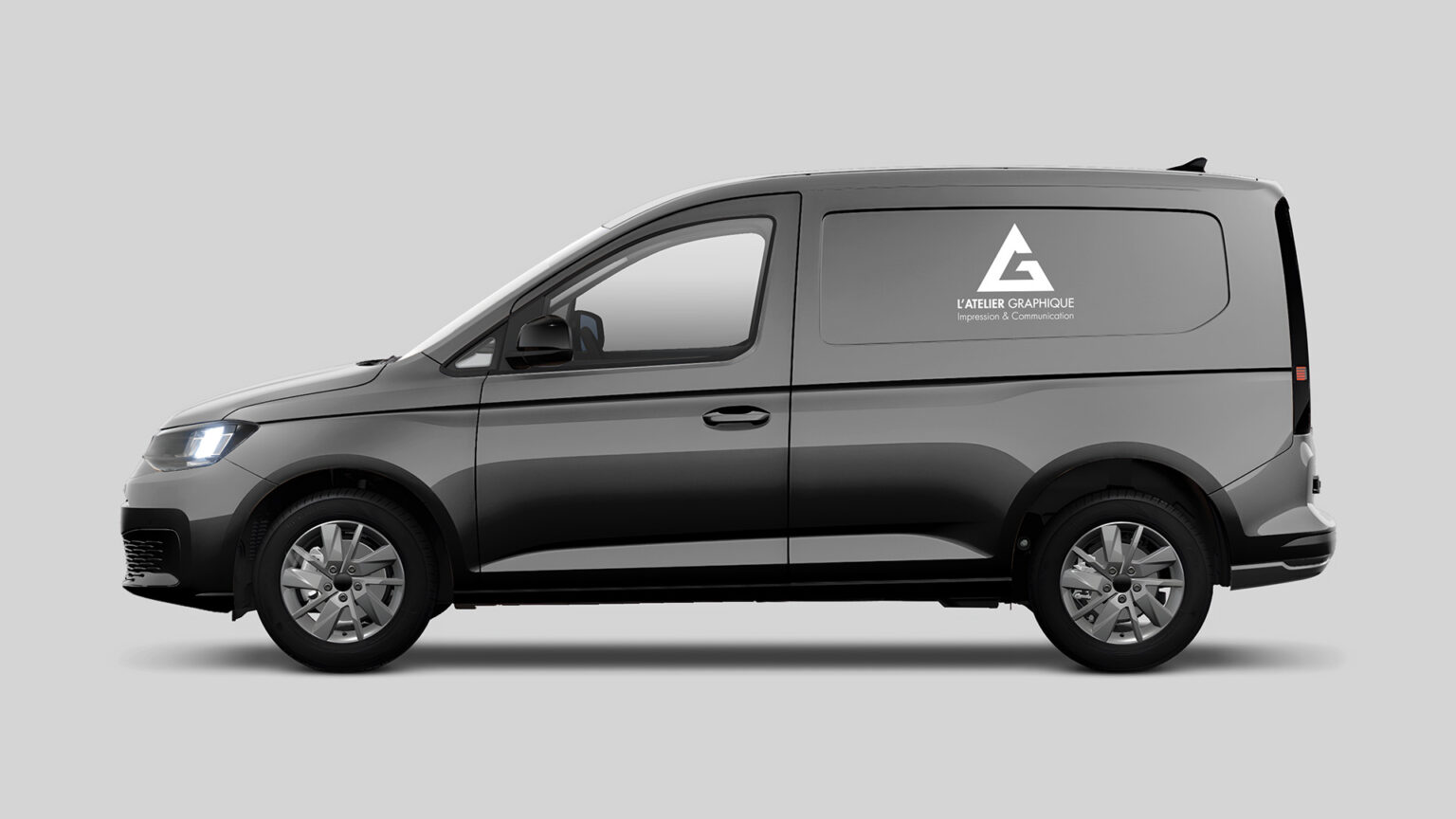 Marquage publicitaire blanc avec le logo de L'Atelier Graphique sur le panneau latéral d'un véhicule utilitaire gris