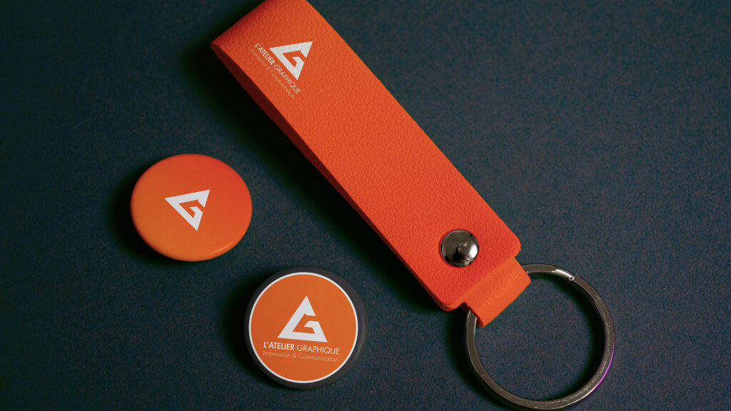 Objets promotionnels personnalisés avec un porte-clés en simili-cuir orange et deux badges publicitaires ronds.